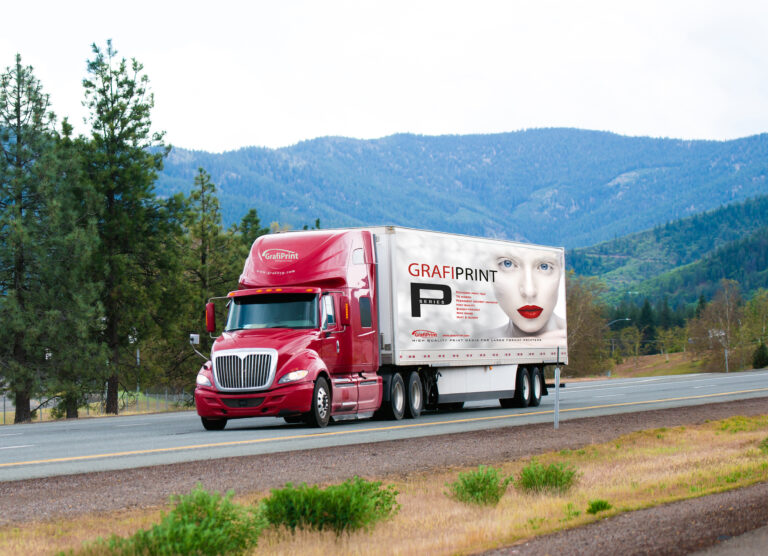 Red modern semi truck with dry van trailer moving by divided highway I-5 in California